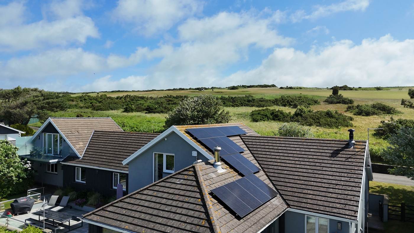 Drone photo of black solar panels split across three roof pitches of a coastal home