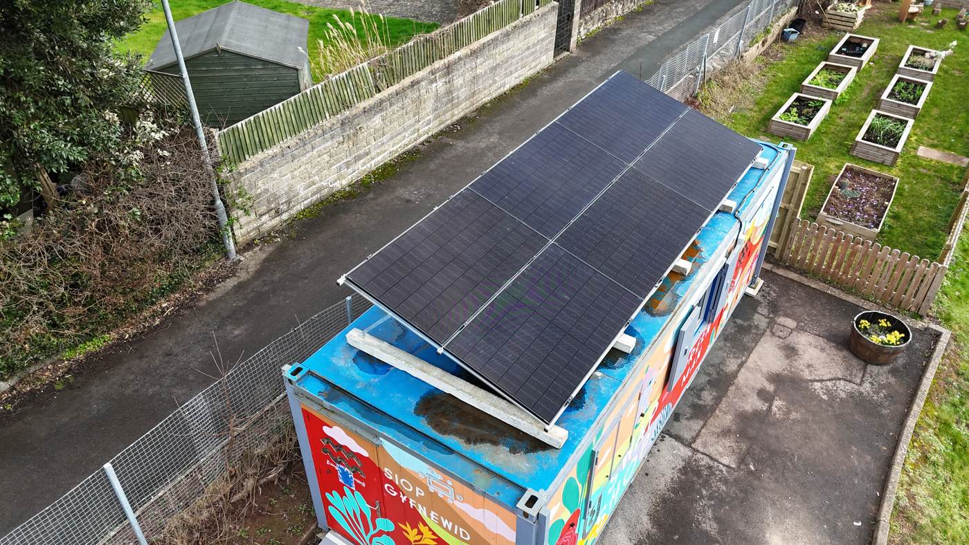Drone photo of tilt-frame solar panels on a community swap-shop container beside allotment beds